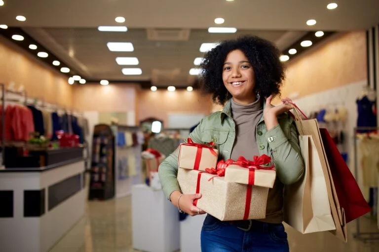 Jovem negra sorri ao carregar caixas de presentes e compras.