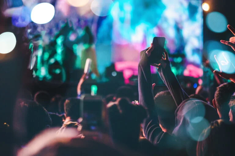 Braços de pessoas para o alto segurando celulares, em plateia de um show a noite.